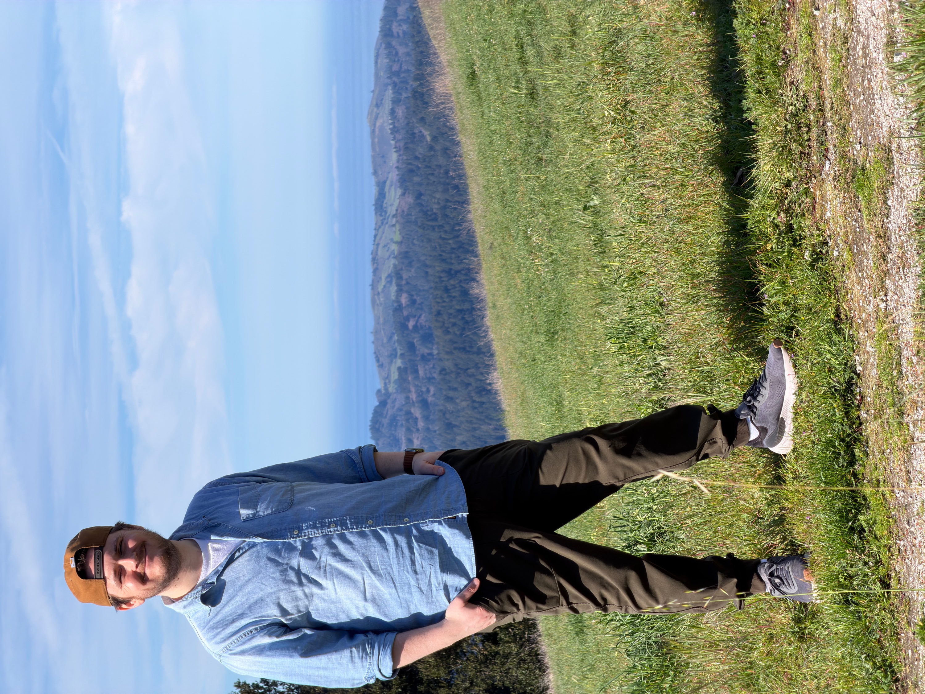 Brian McGovern standing on a grassy hillside overlooking hazy hills and the ocean in the distance